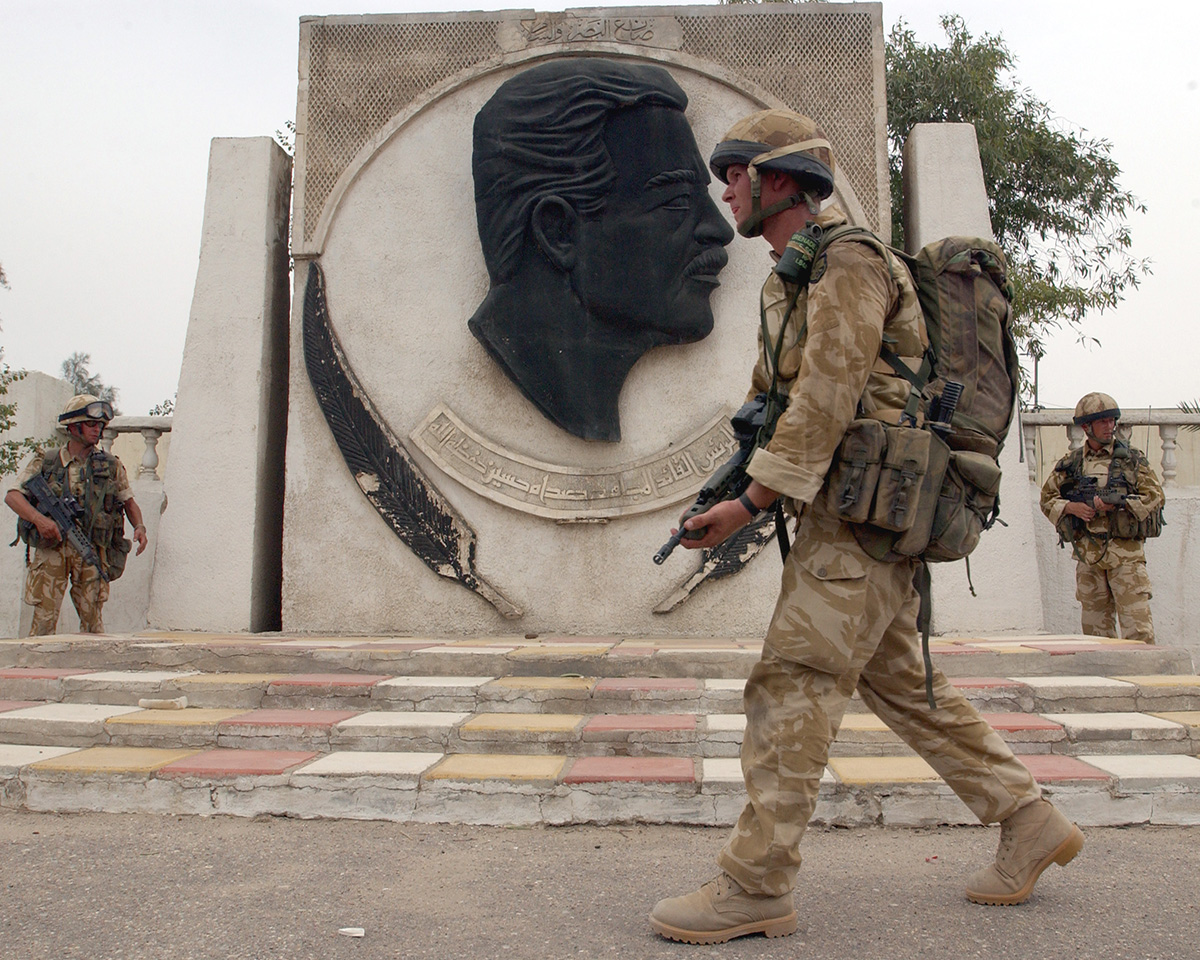 A soldier walks past a monument to Saddam Hussein during a patrol through the streets of Basra, 2003